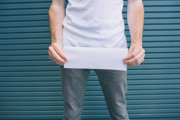 Cut view of man standing and holding blank page above his pants. Guy has problems with urine. Isolated on striped and blue background. — Stock Image Cut view of man standing and holding blank page above his pants. Guy has problems with urine. Isolated on striped and blue background. Stock Photo