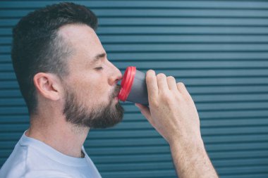 Adam plastik bardak kahve içiyor. Gözleri kapalı tutuyor. Çizgili ve mavi arka plan izole.