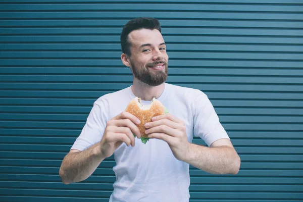 Milá osoba je v rukou držel velký burger a usmíval se na kameru. On je šťastný. Isolateed na pruhované a modré pozadí. — Stock fotografie