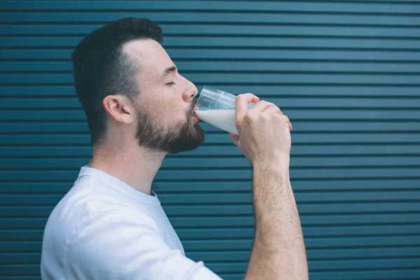 Фото человека, пьющего молоко из стекла. Он держит глаза закрытыми. Изолированный на полосатом и синем фоне . — стоковое фото