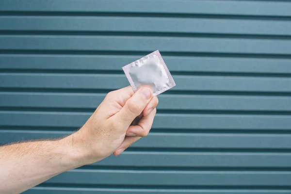 Uma foto de homem segurando mão preservativo embalado. Isolado em fundo listrado e azul . — Fotografia de Stock