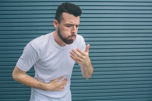 Hasta adam kusma. Bunu önlemek çalışıyor. O stomack bir yandan ve ağız yakın başka bir tutar. Çizgili ve mavi arka plan izole. — Stok fotoğraf