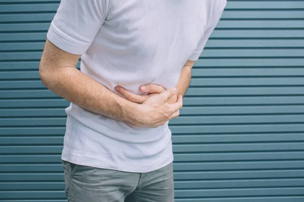 A picture of mans body. Guy is standing and holding hands on stomack. He feels bad. Isolated on striped and blue background. — Stock Photo, Image