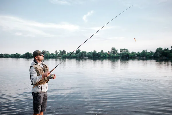 Sığ ve balık tutma ayakta fishaerman bir resim. O sinek çubuk tutar. Adam yukarı ve ileri görünüyor. Sakin.