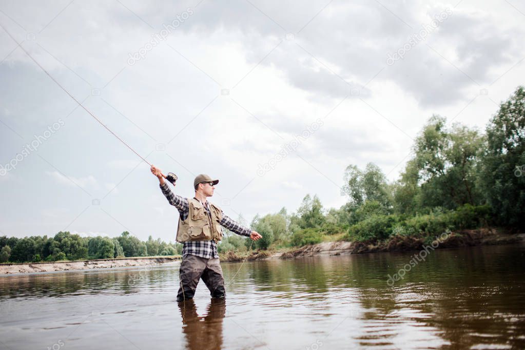 A picture of man holding up fly rod in right hand. He is standing in shallow water and looking straight. He is ready to throw part of spoon with baits in it to catch fish.