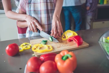 Renkli ve lezzetli yemekler masanın üzerinde yatan bir resim. Orada biber, domates salatalık. Hepls anne yeşil sebze kesmek için onun kızı.
