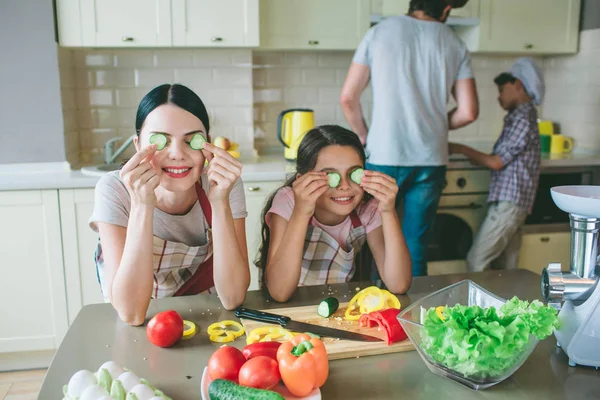 Αστεία κορίτσια παίζουν με τα τρόφιμα. Τους κρατά στρογγυλά κομμάτια αγγούρι όπου etes και χαμόγελο. Τα κορίτσια έχουν ένα διάλειμμα. Αγόρια εργάζονται στο φούρνο. Μαγειρεύουν το φαγητό. — Φωτογραφία Αρχείου