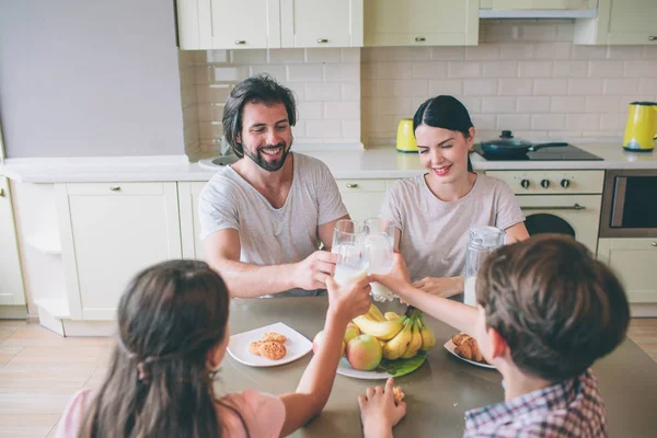 Μέλη μιας οικογένειας καθίσει στο τραπέζι και κρατήστε ποτήρια γάλα μαζί. Αυτοί χαμογελαστός. Η οικογένεια έχει πρωινό. — Φωτογραφία Αρχείου