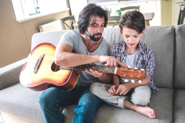 Oğlu ile Divan istting adamdır. O gitar tutar. Adam iplerde işaret ediyor. Çocuk baktığı. Onlar konsantre.