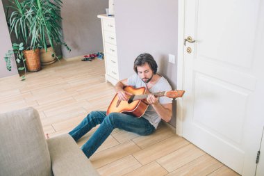 Yalnız katta oturan ve gitar çalmak gy bir resim. O duvara yaslanmış. Adam kendini eğlenceli.