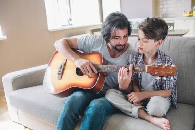 Adamın oğlu nasıl gitar öğretim resmi. Bu tutar ve sert parmaklar hissediyorum görünüyor. Çocuk çok baba yakın oturuyor ve baktığı. Konsantre.