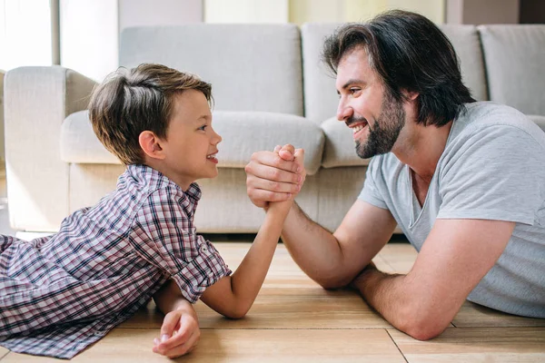 Una imagen positiva y agradable de padre e hijo tumbados en el suelo y tomándose de las manos. Están jugando. . — Foto de Stock