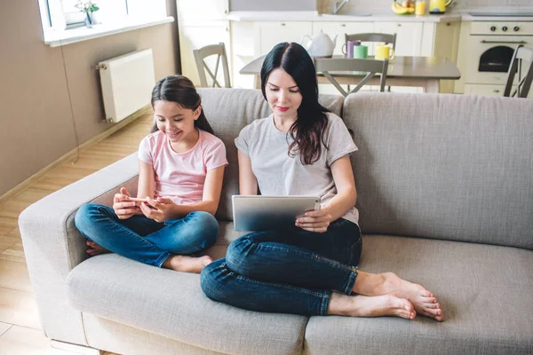 Kız kanepede oturan ve okuma vardır. Kız ellerinde telefon varken kadın tablet tutar. Konsantre görünüyorlar.