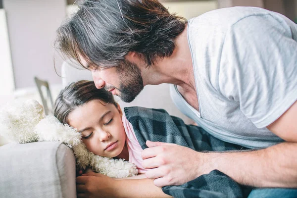 Flickan har somnat. Hon är täckt med filt. Hennes pappa sitter förutom henne. Han kommer att kyssa barn. — Stockfoto