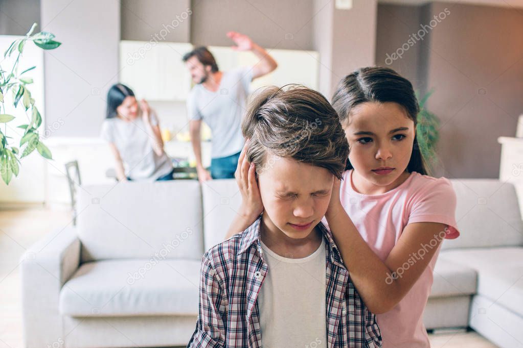 Girl stands behind her brother and keeps his ears closed with hands. Boy is terrified. He has eyes closed. Woman is trying to protect herself. Guy is going to beat her. He holds his hand up.