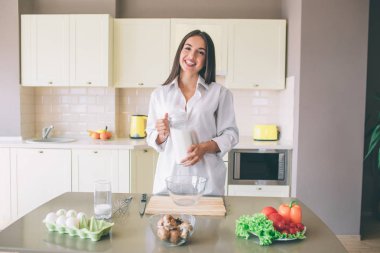 Güzel ve güzel esmer ile yemek masada duruyor ve cam süt ile tutar. Kamera ve gülümsüyor üzerinde görünüyor. Kız beyaz bluz giyer.