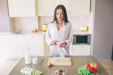 Güzel kız masada duruyor ve bıçak ve yumurta tutar. O bakıyor. Kız bir yumurta kırmak için gidiyor.