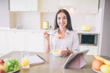 Mutlu ve olumlu kız kamerada gülümsüyor. O bir kaşık süt ve Mısır gevreği ile tutar. Mutfakta oturuyor.