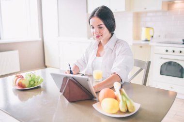 Esmer tablo ve wokring oturuyor. Not defterinde yazıyor. Ayrıca kız görünüyor ve tablet dokunur. Biraz gülümsüyor.