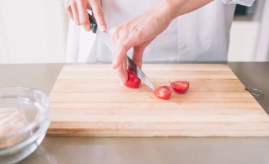 Holding ve cerry domates kesme kadının el kapatın. Ahşap tahta üzerinde bıçakla yapıyor.