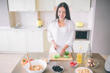 Keyifli ve mutlu genç kadın anlamına gelir ve mutfakta aşçılar. Ahşap tahta üzerinde marul keser. Kız erkek ingrediends tablo vardır..