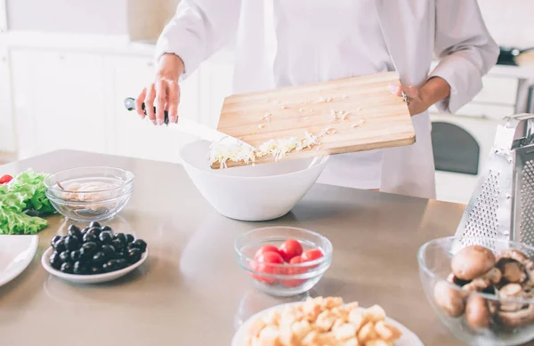 Skär syn på kvinnans händer att sätta måltid i vit skål. Hon använder kniv för detta. Flickan är matlagning. — Stockfoto
