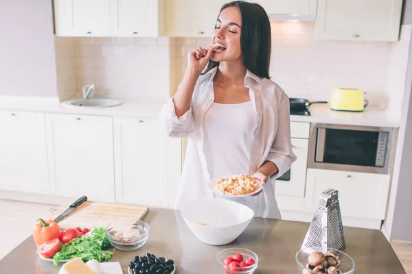 Uma foto de menina de pé e degustação pedaço de pão frito. Ela segura o prato na mão. Menina está cozinhando salada . — Fotografia de Stock