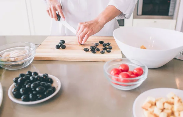 Skär syn på kvinnans händer och skär oliverna på träskiva med kniv. Hon matlagning sallad. — Stockfoto