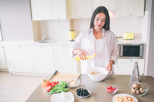 Menina agradável está cozinhando na cozinha. Ela está misturando ingredientes para salada em tigela. Menina é calma e concentrada . — Fotografia de Stock