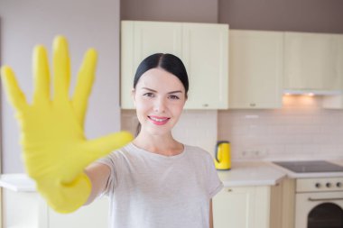 Mutlu ve olumlu esmer mutfakta duruyor ve ellerini sarı torpido gözünde gösterir. Kamera ve gülümsüyor üzerinde görünüyor. Kız mutlu görünüyor.