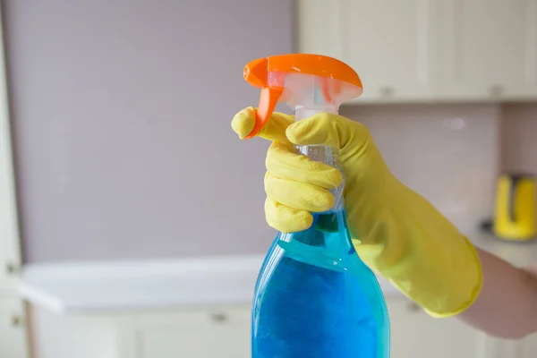 A picture of hand in yellow glove holding spray bottle with blue liquid. Finger is going to push the hook.