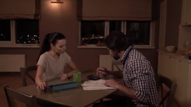 Erkek ve kadın masaya oturabiliriz. Hesap makinesi ve merak saymak. Kız ona bakar. Sakin o. Kız ellerini tablet ve Kupası yakın tutar. Adam açıklayan. O kağıtları görünüyor.