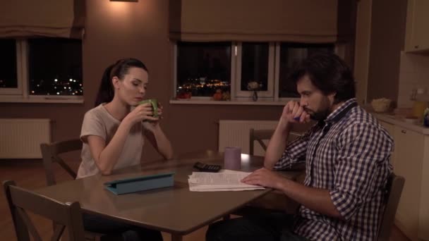 怒って男性と女性は、テーブルに座る。彼らは考えています。女の子のカップから飲むと夫。彼は論文を見て、口の近くに拳を保持します。男が考えています。心配しています。. — ストック動画