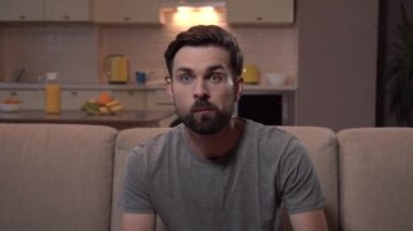 Sakallı adam televizyon izliyor. O gergin. Adam patlamış mısır yiyor ve elini uzatır. O endişe olduğunu.