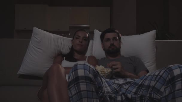 Hombre y mujer están sentados en la oscuridad en el sofá y viendo películas. Comen palomitas de maíz. La chica empieza a dormirse. Se miran y siguen mirando. . — Vídeos de Stock