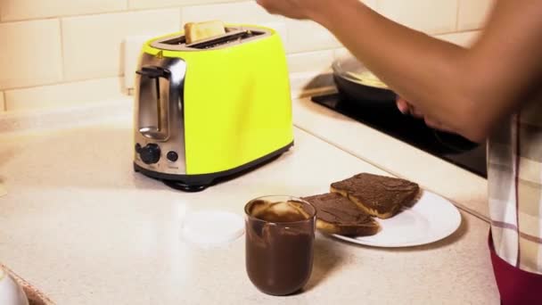 Die Kamera ist auf Mädchenhände gerichtet. Sie nimmt einen Toast aus dem Toaster. dann nimmt Mädchen nife und holt etwas Nutella aus dem Glas und heraus auf gebratenem Brot. sie schmiert es auf Toast. — Stockvideo