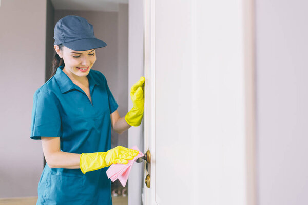 Happy and cheerful woman stands and holds the white door. She cleans it with rag. Girl looks down. She works with pleasure.