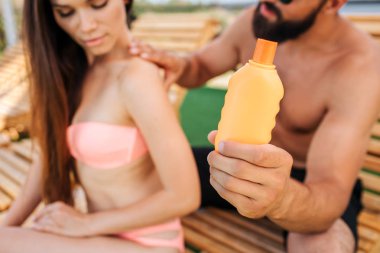 Ciddi adam ve kız otur. O turuncu şişeden onun omuz ve sırt sunproof kremi koyar. O tepeden bakıyor.