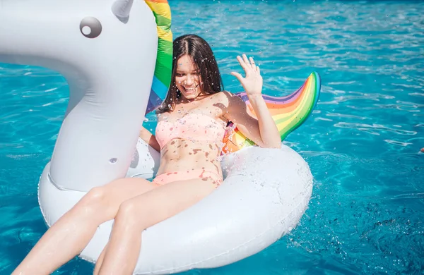 Attractive and beautiful woman is lying on air mattress in swimming pool. She holds hand in air. Girl protects herself from water splashing. She has some fun. — Stock Photo, Image
