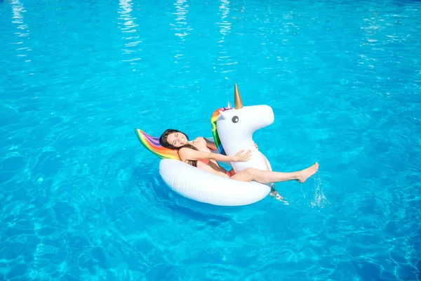 Happy and positive young woman is lying on air mattress in the middle of swimming pool. She waves with hes leg making water splashing. — Stock Photo, Image