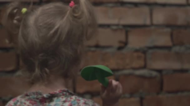 Small blonde girl stands in front of wall and hold green shovel. She knocks on brick wall two times. Girl looks at it. — Stock Video