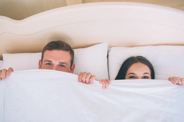 男と白い毛布の下で顔を隠す女の画像。彼らは 1 つのベッドで一緒に横たわっています。Peple はまっすぐ前方を見ています。. — ストック写真