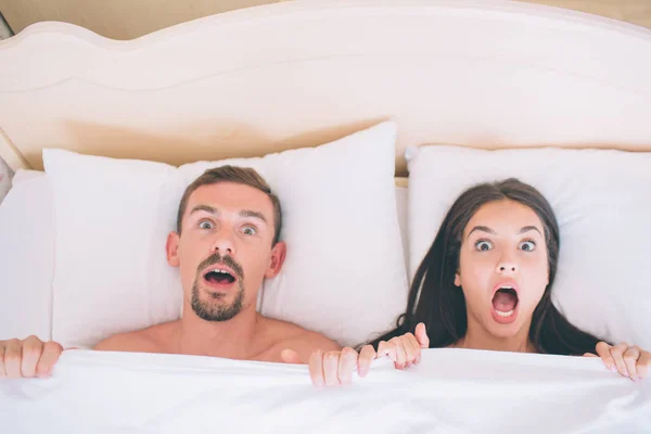 不二と terified の男性と女性は、ベッドに横たわっています。彼らは白い毛布で覆われています。人の手でそれを保持します。彼らはまっすぐカメラを. — ストック写真