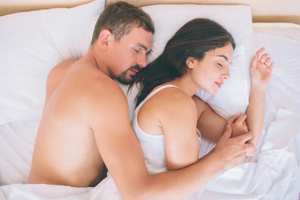 Casal lindo está deitado na cama juntos. Eles dormem. O tipo está deitado atrás da rapariga. Ele segura a mão dela. Parecem calmos e pacíficos . — Fotografia de Stock