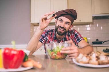 Bir adam güzel bir resim anlamına gelir ve tabloya eğilir. O siyah zeytin bir elinde tutan ve kase üzerinde başka bir tutar. Adam mutlu ve memnun görünüyor.