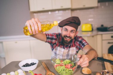 Nice ve positice Şef mutfak masa ve beklemeler şişe yağı, duruyor. Bir kısmı salata bir kase içine dökülen. O mutlu ve heyecanlı görünüyor.