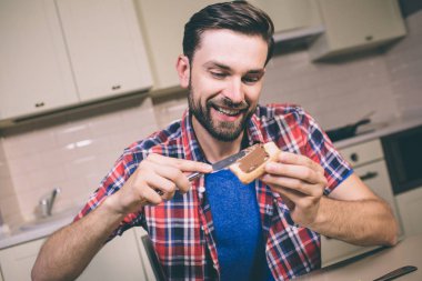 Yakışıklı adam tablo ve gülümsüyor oturur. Tost krem koyar. Adam mutlu ve aç görünüyor.