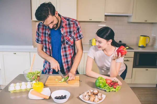 Mutlu çift birlikte kalıyor. Parçalar halinde salatalık keser. O oturur ve baktığı. Kız kırmızı biber sol elinde tutar. Sebze tablo üzerinde bir yeri vardır.