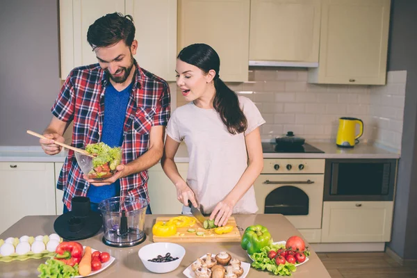 Heyecanlı kız masada duruyor ve sarı biber keser. Adam tutarak salata ile bowl görünüyor. Tahta kaşıkla malzemeler karışımları. Birlikte cook. — Stok fotoğraf