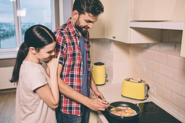 Güzel çift birlikte soba duruyor. Gıda tavada ateşler. Kız adamın arkasında duruyor ve ona eğilir. Her ikisi de pan aşağı bakmak.